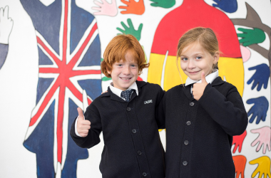 Two primary aged children smiling, giving thumbs up with a decorative background with international flags.