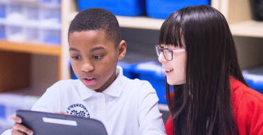 A female and a male student looking at a tablet in class.